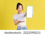 Young Asian woman holding phone with cheerful face on yellow background