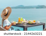 Dinner with sea view in luxury hotel. Woman in straw hat near swimming pool, eating food and enjoy ocean view. Dinner table on tropical vacation. Back view. Concept of travel, holidays, weekend.