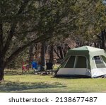 Family camping tent with folding chairs under tree shade at camping site in national park of Oklahoma, America. Wintertime outdoor and recreational activity