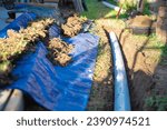 Small photo of Blue tarp, black mixing tub container with dirt, underground PVC pipe buried in trench installation, rainwater drainage system connected gutter of residential house, Dallas, Texas, USA. Piping sewer