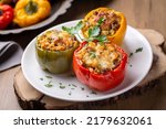 Stuffed peppers, halves of peppers stuffed with rice, dried tomatoes, herbs and cheese in a baking dish on a blue wooden table, top view. (Turkish name; biber dolmasi)