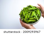 The child's hands hold a white cup full of pea pods, the daily norm of legumes for children.