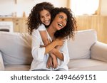 Happy Latin mother and daughter bonding in living room, laughing and having fun together, copy space. Family, affectionate concept