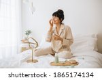 Happy woman doing routine skin care at home with beauty products. Woman sitting on bed at home and applying face cream.