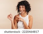 Small photo of Woman smiling happily while pointing at the copper IUD in her hand. Young woman choosing a non-hormonal method as a form of contraception. Woman taking control of her reproductive health.