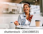 Small photo of Happy post-graduate student working on her assignment at a cafe, browsing with her phone. Young woman enjoying the quiet atmosphere in a coffee shop as she engages in her school work.