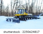 A snow plougher of ski trails stands on a platform near the forest on a winter day