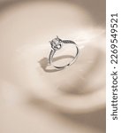Small photo of White gold ring with diamond on beige background with shadows. Still life and creative photo