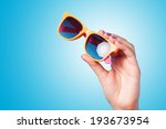 Hand holding sunglasses on blue background