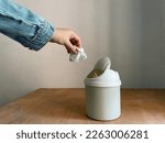 Female hand throwing away a crumpled tissue in small dustbin above wooden table