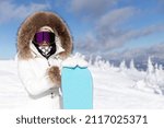 Small photo of winter, leisure, sport and people concept - Girl snowboarder stands with snowboard on mountain's top on sunrise backdrop. woman in fur hood and snowboarding goggles