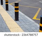 Yellow tactile pavement for the blind on the bus stop. Bus stop with traffic road bollards protecting pedestrian sidewalk. Concept traffic restriction, no access to drive. Yellow, black pillar bumper.