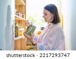 Young woman in kitchen with containers jars of food, holding jar of dry bay leaves