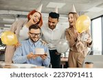 Small photo of Young man is going to blow candles on cake and make a wish while celebrating birthday with colleagues. Colleagues celebrating a birthday in the office