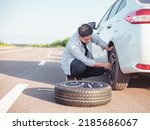 Small photo of Handsome Asian man checking the punctured tyre on his car loosening the nuts with a wheel spanner before jacking up the vehicle in street. Men hold rubber to repair. Change tire. broken car concept.