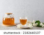 front view of a glass teapot with jasmine tea and a modern cup with a natural delicious drink. gray background. tea time