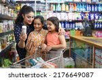 Small photo of Indian happy family of mother and daughters shopping in a hypermarket. They are purchasing grocery products as per their needs in a supermarket. Joyful Indian family purchasing in Grocery store.