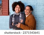 Happy cheerful black adult daughter and mother with broad smile embracing each other outside humble home Togetherness, family, support concept.