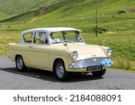 Small photo of Birkhill, Scotland - JUNE 25, 2022: 1961 Yellow Ford Anglia saloon car in a classic car rally en route towards the town of Moffat, Dumfries and Galloway