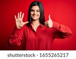 Young beautiful brunette woman wearing casual shirt standing over red background showing and pointing up with fingers number six while smiling confident and happy.