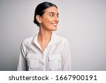 Young beautiful brunette woman wearing casual shirt over isolated white background looking away to side with smile on face, natural expression. Laughing confident.