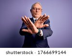 Grey haired senior business man wearing glasses and elegant suit and tie over purple background Rejection expression crossing arms and palms doing negative sign, angry face