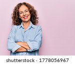 Small photo of Middle age beautiful woman wearing casual denim shirt standing over pink background happy face smiling with crossed arms looking at the camera. Positive person.