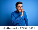 Young handsome man with beard wearing casual sweater and glasses over blue background hand on mouth telling secret rumor, whispering malicious talk conversation