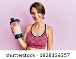Young brunette woman with short hair wearing sport clothes drinking a protein shake looking positive and happy standing and smiling with a confident smile showing teeth 