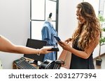 Young hispanic customer woman smiling happy paying using smartphone at clothing store.