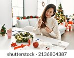 Middle age hispanic woman painting christmas pineapple decor sitting on the table at home