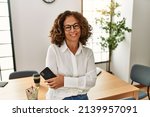 Middle age hispanic woman smiling confident holding smartphone at office