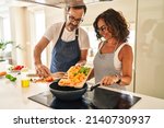 Middle age hispanic couple smiling confident pouring food on frying pan at kitchen