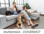 Small photo of Young hispanic couple with dogs relaxing at home smelling something stinky and disgusting, intolerable smell, holding breath with fingers on nose. bad smell