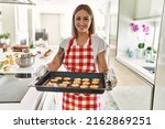Young caucasian girl smiling happy holding tray with cookies at the kitchen.
