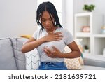 African american woman examining breast sitting on sofa at home