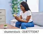 Young african american woman using smartphone sitting on sofa at home