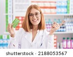 Small photo of Young redhead woman working at pharmacy drugstore holding birth control pills smiling happy pointing with hand and finger to the side