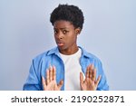 Small photo of African american woman standing over blue background moving away hands palms showing refusal and denial with afraid and disgusting expression. stop and forbidden.