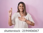 Small photo of Blonde woman standing over pink background smiling swearing with hand on chest and fingers up, making a loyalty promise oath