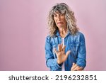 Small photo of Middle age woman standing over pink background disgusted expression, displeased and fearful doing disgust face because aversion reaction. with hands raised