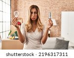 Small photo of Young blonde woman holding led lightbulb and incandescent bulb depressed and worry for distress, crying angry and afraid. sad expression.