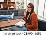 Small photo of Young hispanic woman working as psychology counselor gesturing finger crossed smiling with hope and eyes closed. luck and superstitious concept.