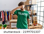 Small photo of Young arab man wearing volunteer t shirt at donations stand covering eyes with hand, looking serious and sad. sightless, hiding and rejection concept
