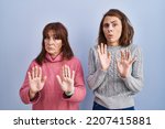 Small photo of Mother and daughter standing over blue background moving away hands palms showing refusal and denial with afraid and disgusting expression. stop and forbidden.