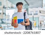 Young hispanic teenager student using touchpad holding books at university