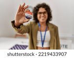 Young hispanic woman smiling confident holding i voted badge at electoral college
