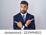 Small photo of Handsome hispanic man wearing suit and tie pointing to both sides with fingers, different direction disagree