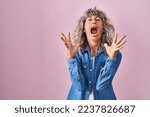 Middle age woman standing over pink background crazy and mad shouting and yelling with aggressive expression and arms raised. frustration concept. 