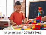 Small photo of Adorable hispanic toddler playing with maths puzzle standing at kindergarten